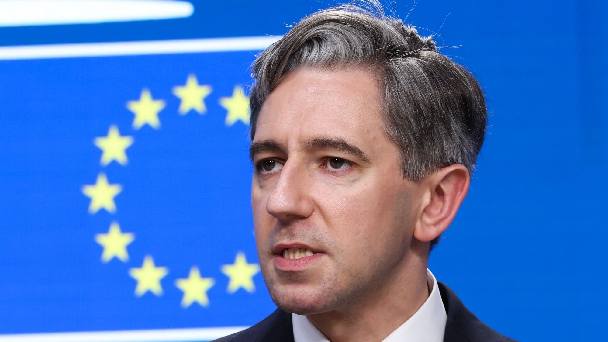 Simon Harris speaks during a news conference, with the European Union flag visible in the background