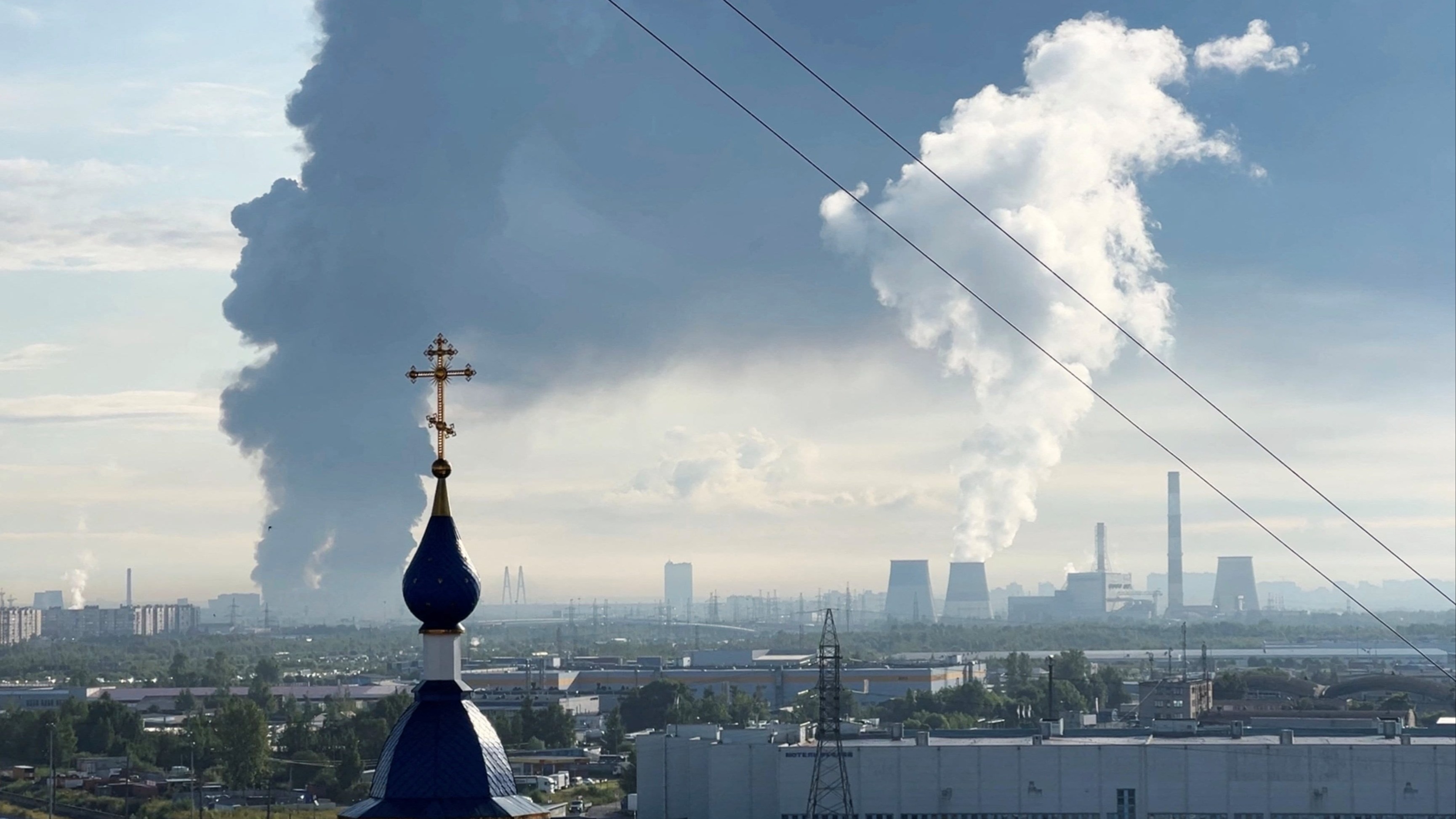 Thick black smoke rises from the Wildberries warehouse in the distance, with a church dome and cross visible in the foreground.
