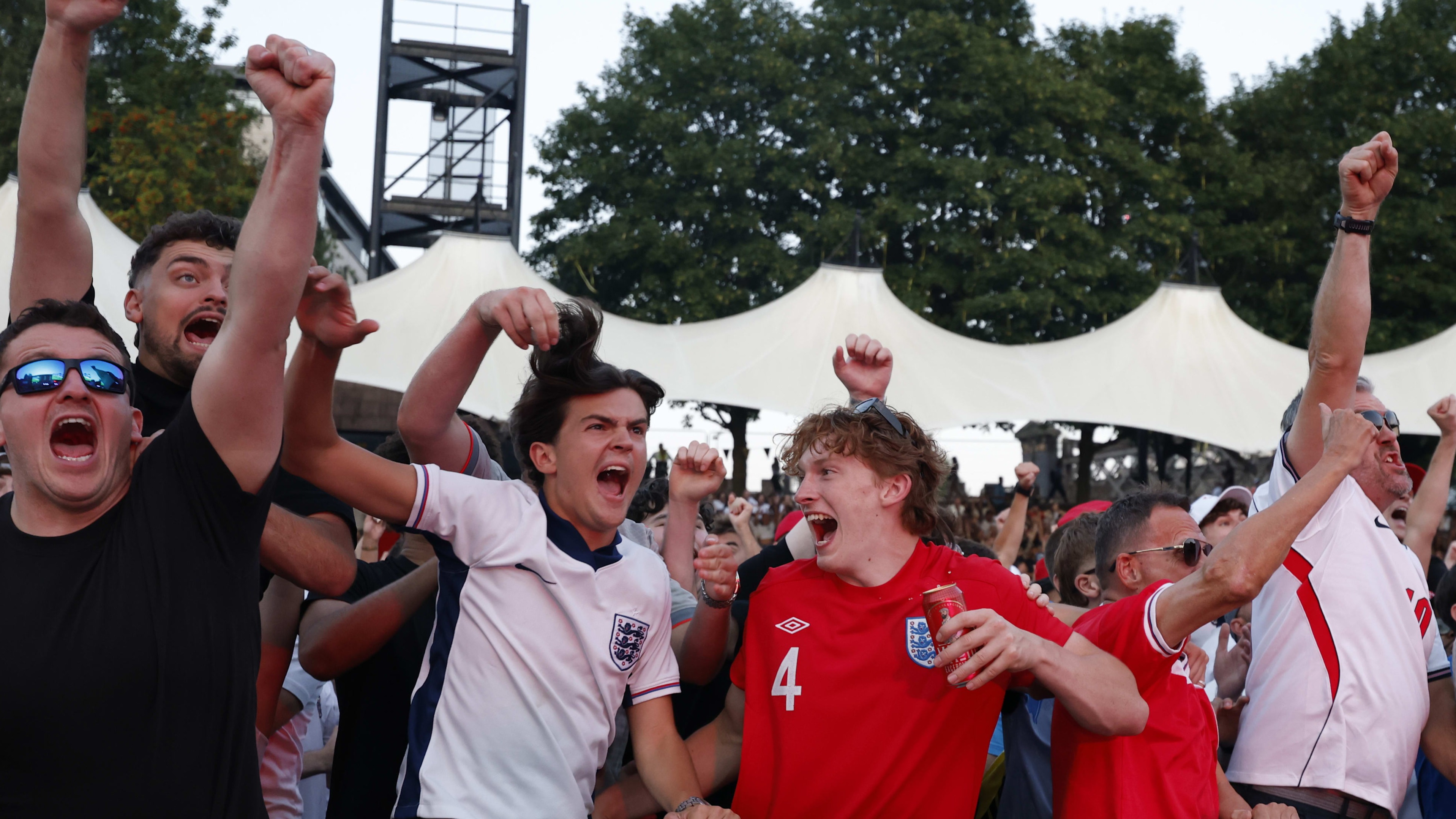England fans wearing team shirts and raising their arms cheer and celebrate during a World Cup semi-final match screening.