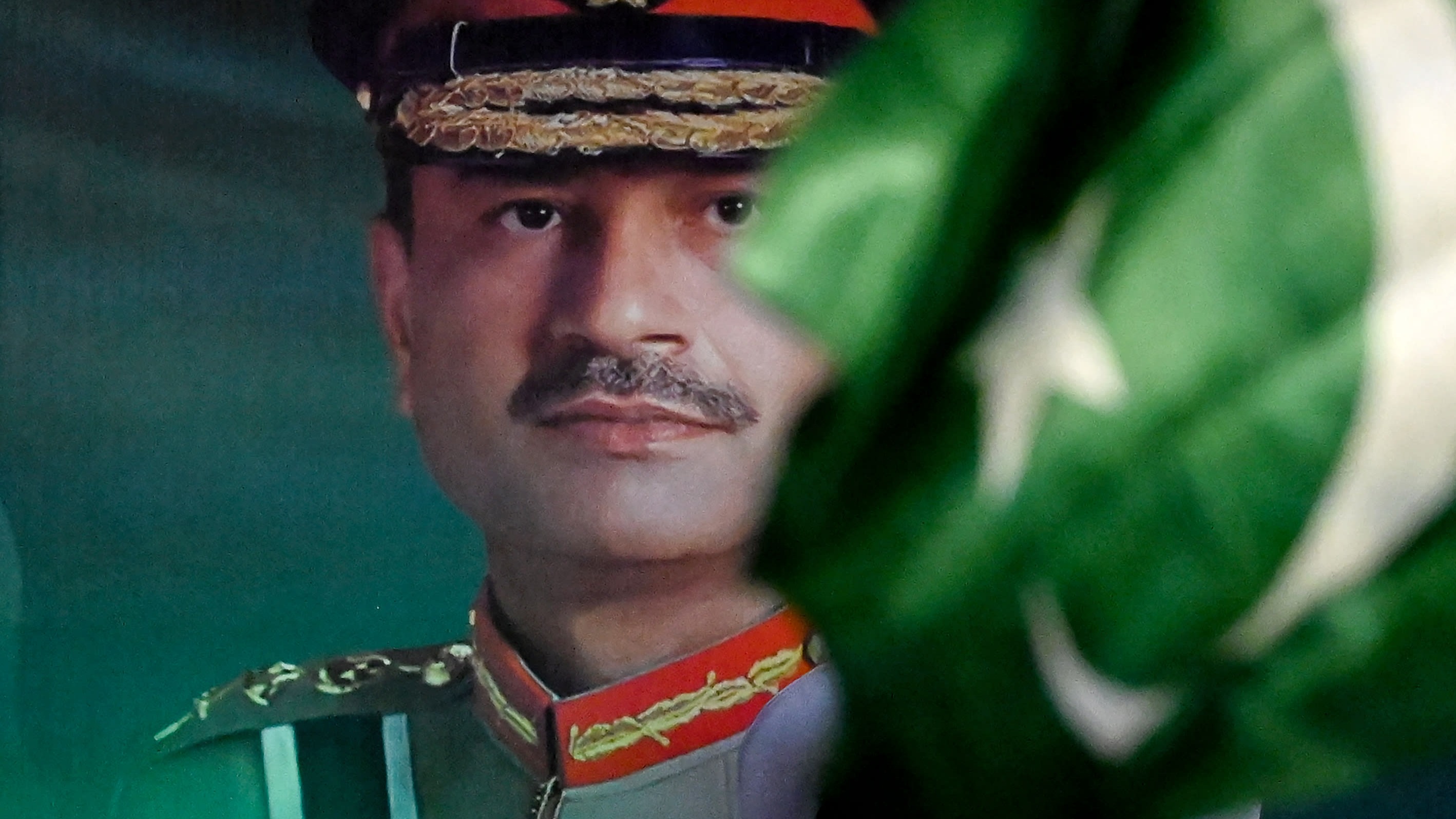 A banner showing Pakistan's Army Chief and Field Marshal Syed Asim Munir, partially obscured by a waving national flag.