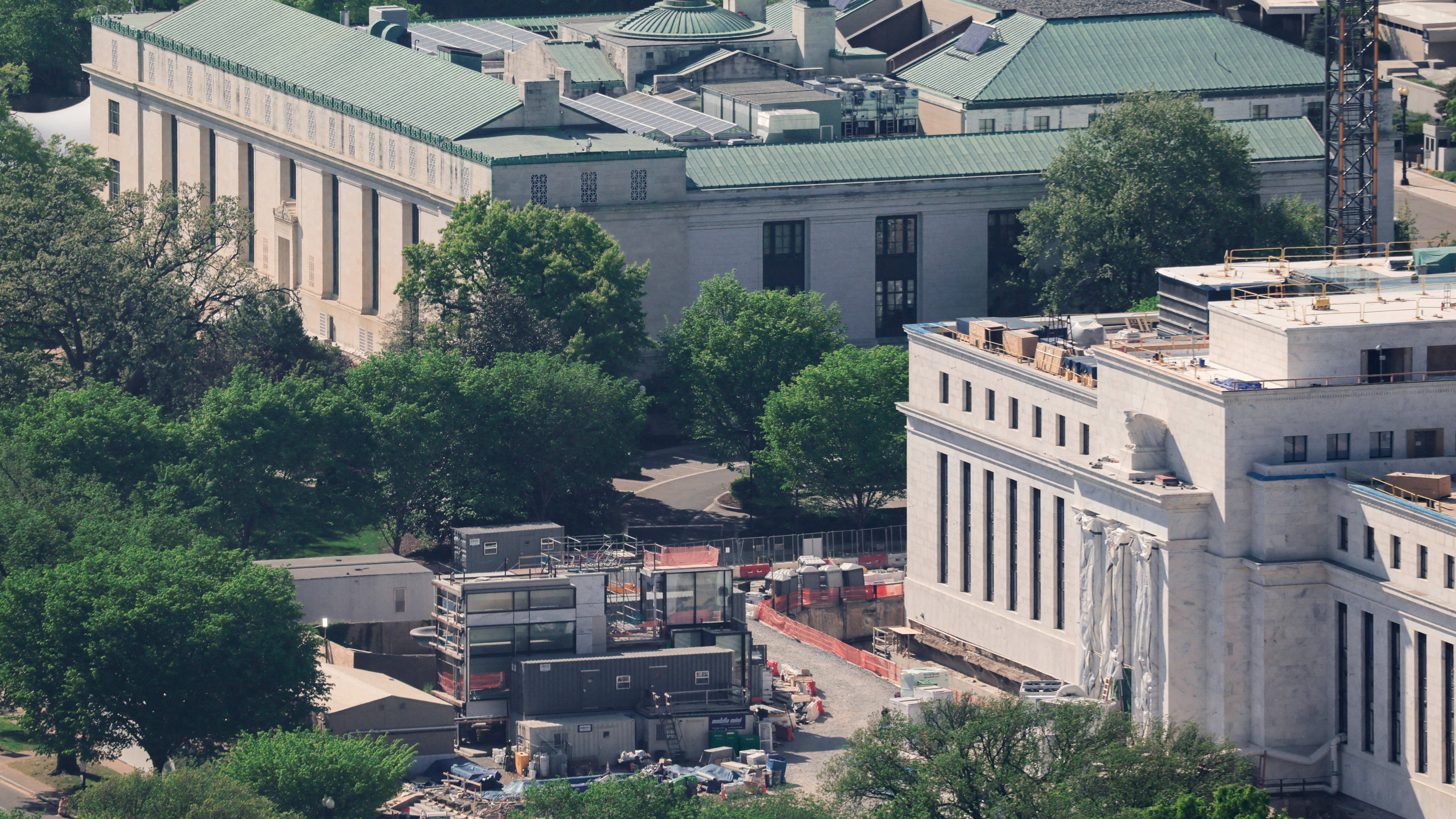 The Federal Reserve building with construction equipment and materials around its exterior, scaffolding, and temporary structures visible.