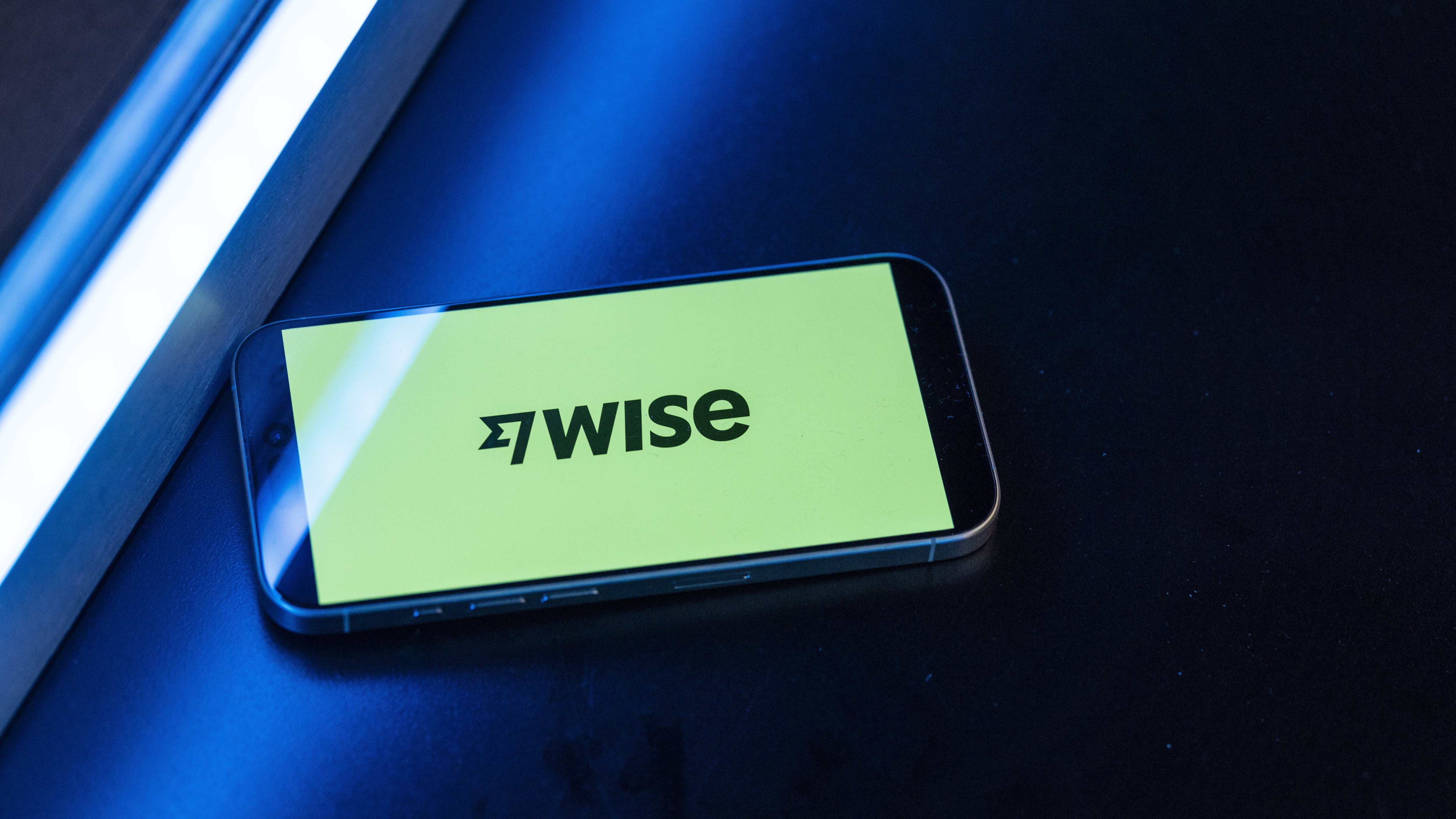 The Wise Plc logo displayed on a smartphone screen with a yellow background, resting on a dark surface.